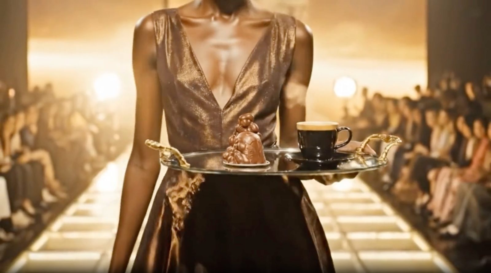 A model presenting a silver tray with a Nespresso coffee and a sculptural chocolate.