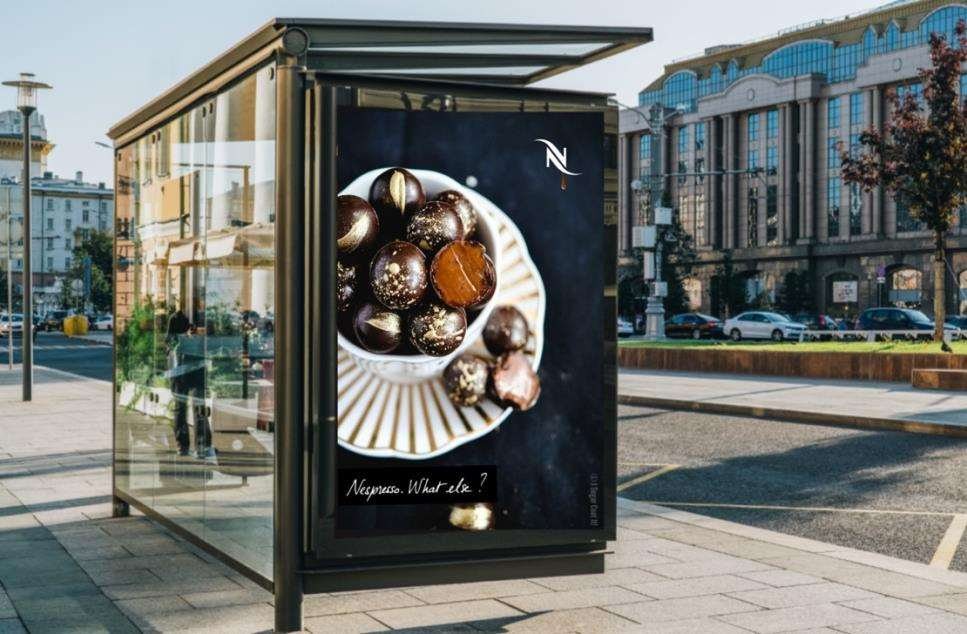 A gold bus-shelter DOOH teaser carrying only the chocolate drop and 'What else?'.