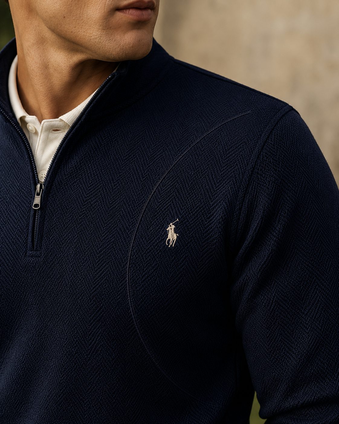 Close-up of a navy quarter-zip, the swing arc traced as a subtle curved seam beside the embroidered pony.